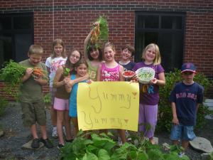 a group of children with a handmade sign and vegetables from a garden